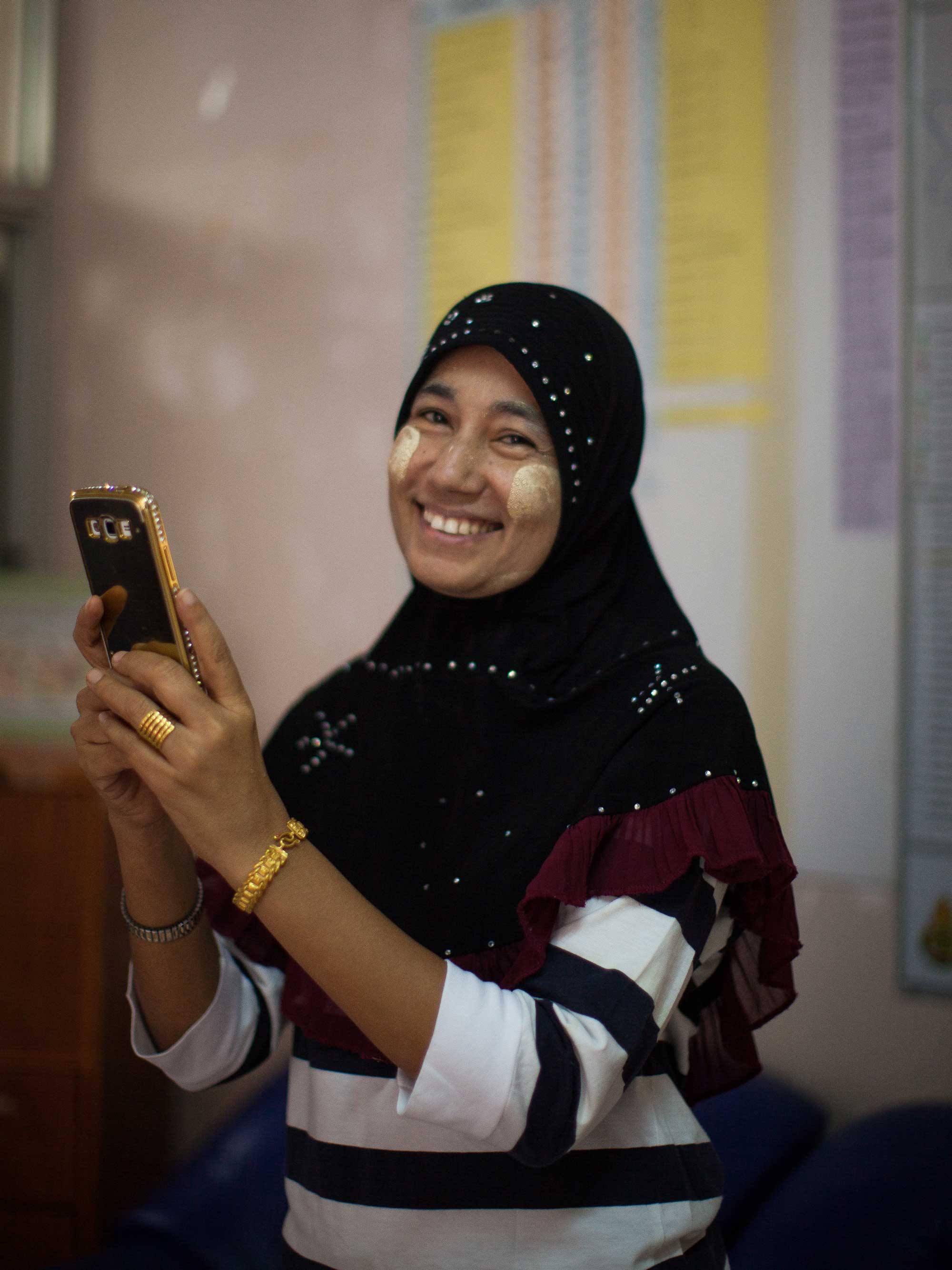 A Burmese refugee smiling while holding a cellular phone. IRC/Kellie Ryan