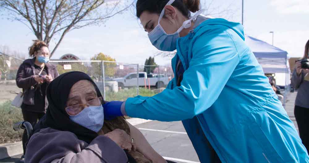 A healthcare worker gives a COVID vaccine to a patient at a mobile medicine clinic. IRC/Dereck Knowles